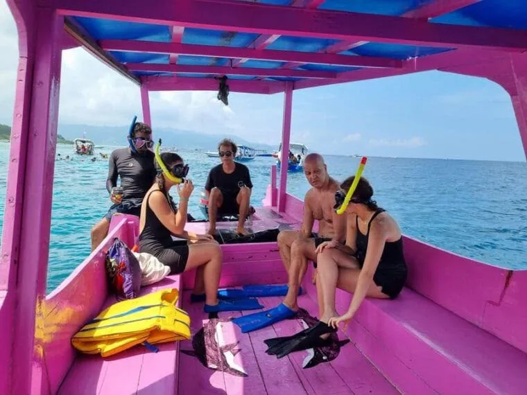 Guests sitting in a traditional pink boat with masks and fins before a snorkeling stop in the Gili Islands
