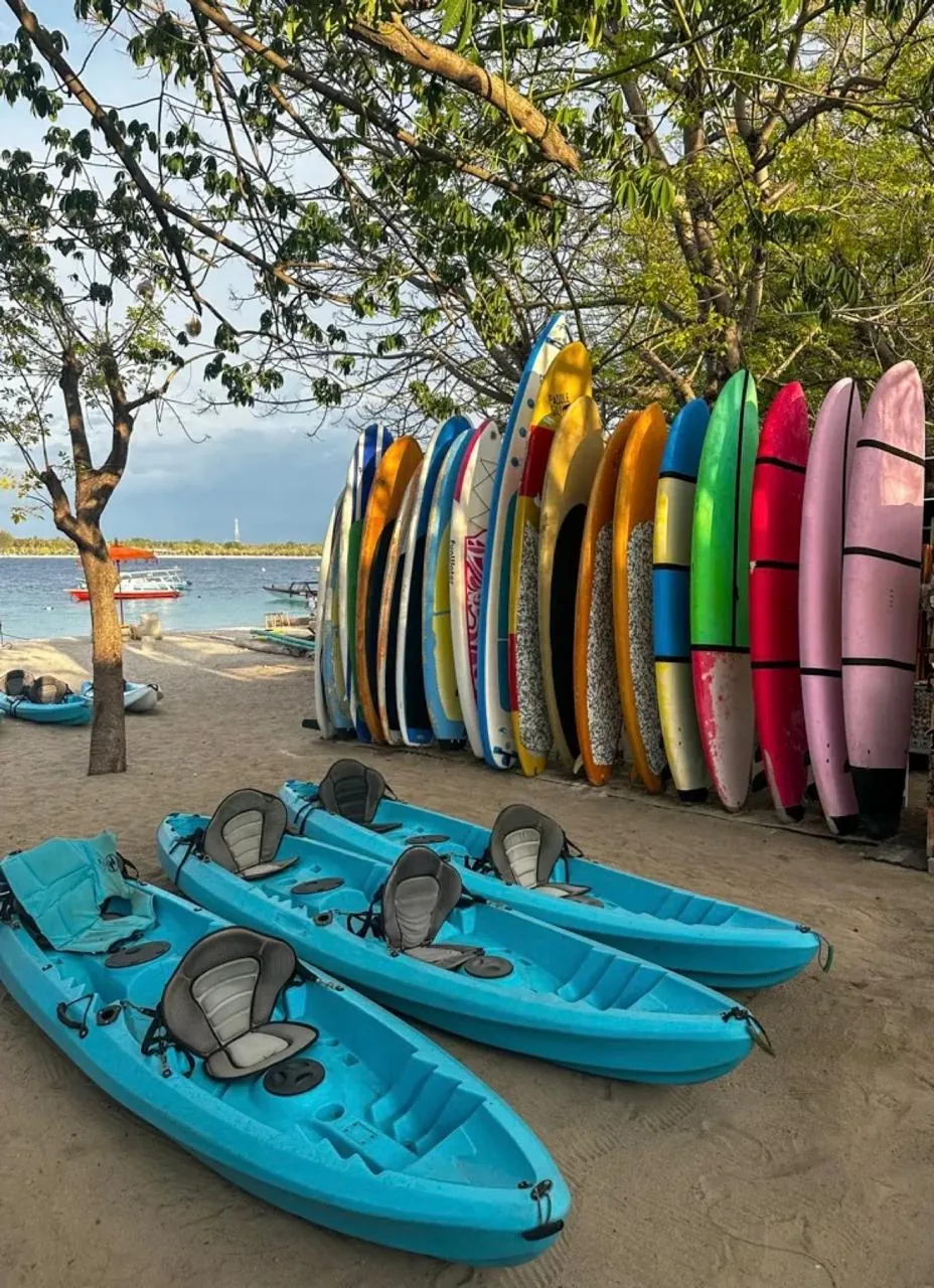 Blue double kayaks and a rack of paddle boards on the beach in the Gili Islands