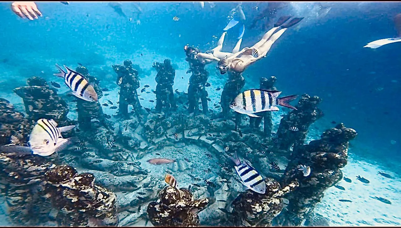 Snorkelers above the ring of underwater statues off Gili Meno, surrounded by tropical fish