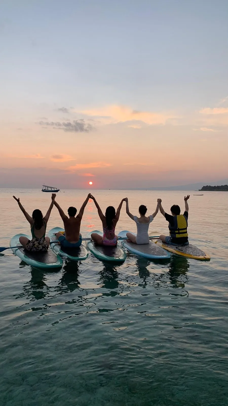 A group of paddlers holding hands on their boards at sunset in the Gili Islands